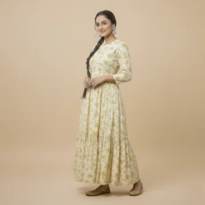 Woman wearing a yellow printed cotton maxi dress with three-quarter sleeves, floral motifs, a tiered hem, and traditional flats.