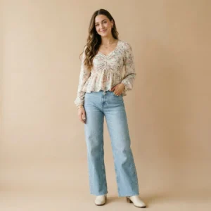 Woman wearing a floral ruched peplum top with a V-neckline and long sleeves paired with light blue wide-leg jeans and ankle boots.