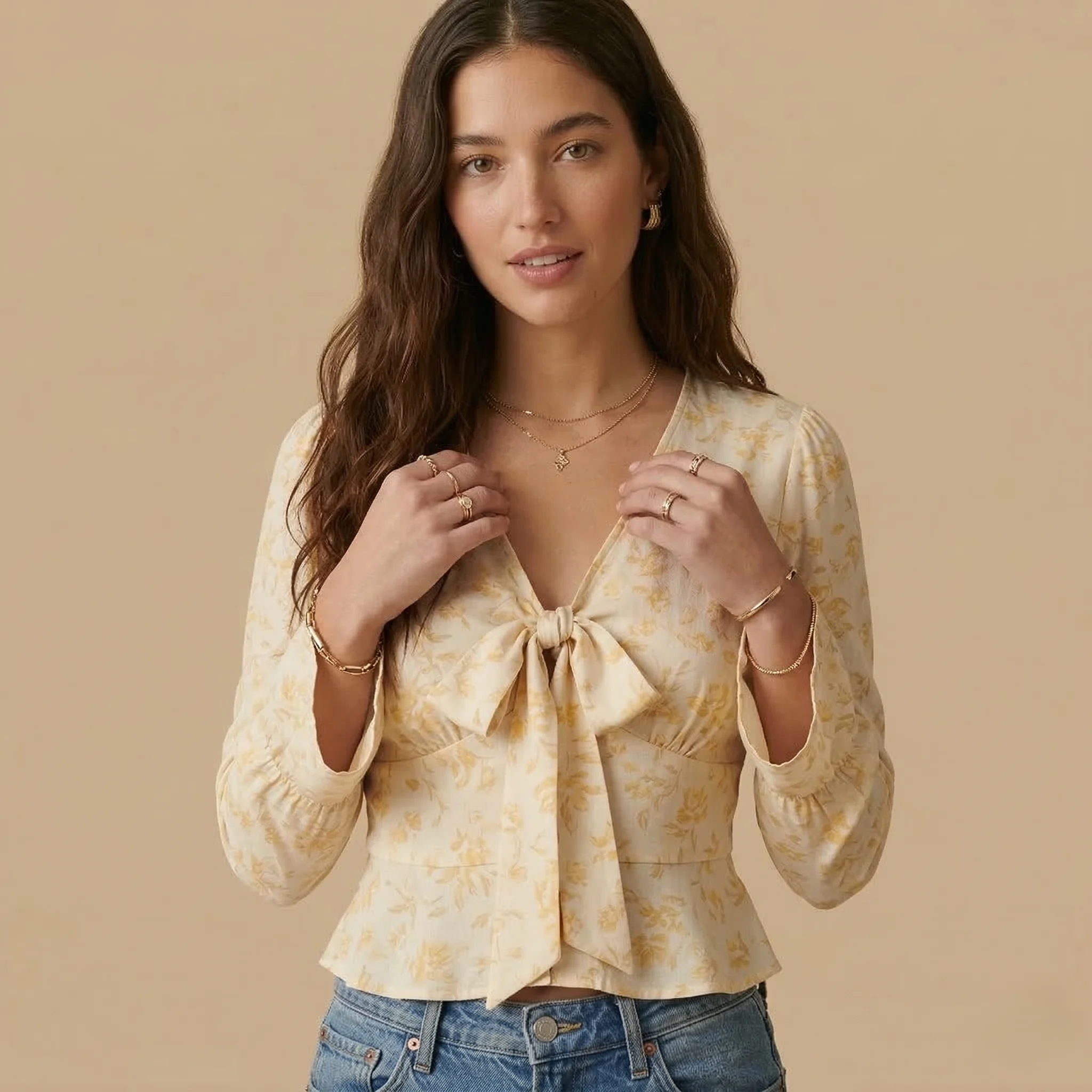 Woman wearing a cream floral bow-front V-neck blouse with long sleeves and light wash blue jeans.