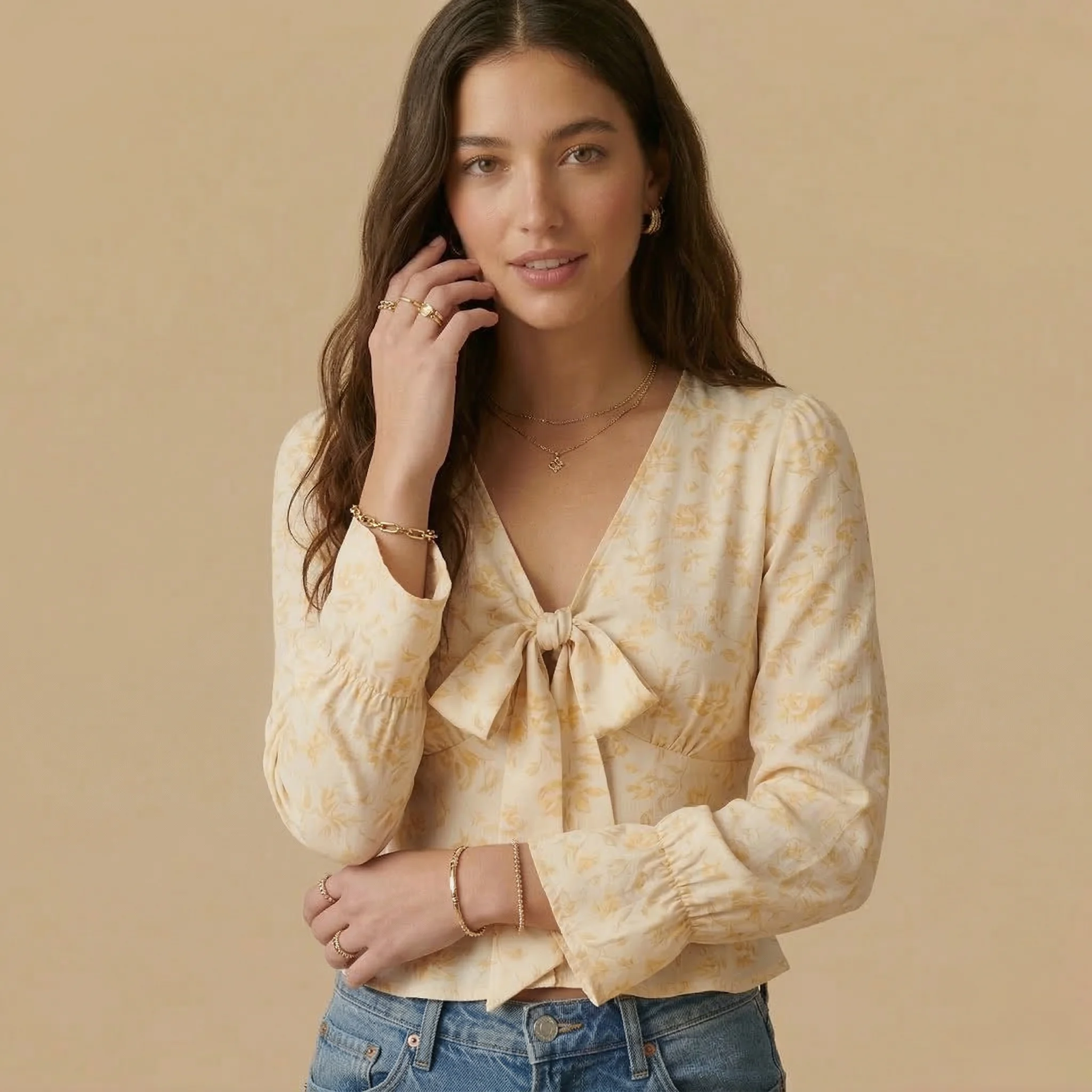 Close-up of a woman wearing a cream floral tie-front blouse with long sleeves and light wash blue jeans.