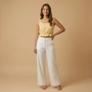 Woman wearing a yellow eyelet embroidered crop top with tie-shoulder straps and a ruffle hem paired with white wide-leg trousers.