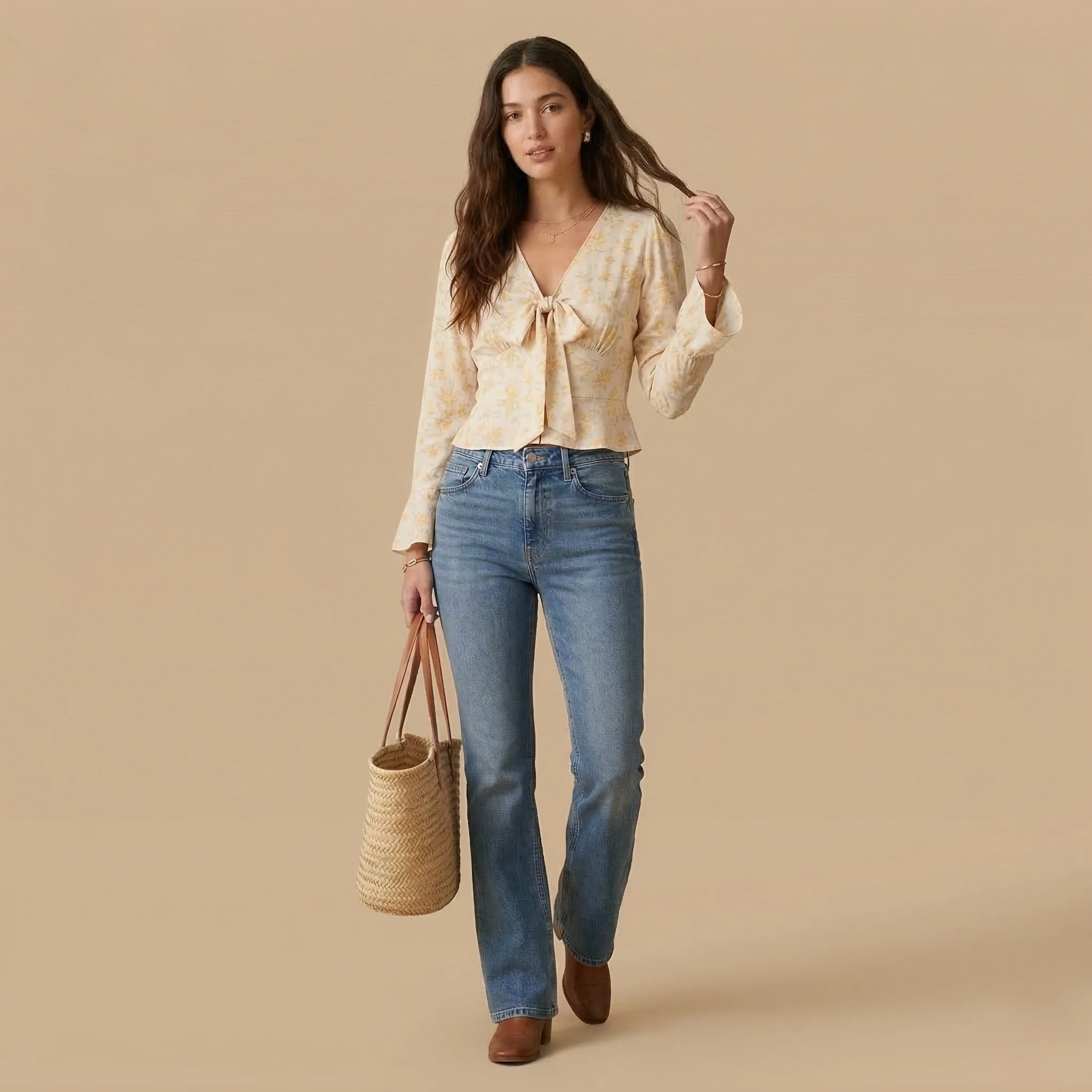 Woman wearing a cream floral tie-front blouse with light wash straight-leg jeans, brown ankle boots, and a woven tote bag.